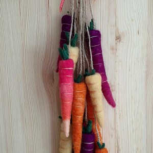 May include: A felt carrot garland with a burlap and red ribbon bow. The garland features a variety of colors, including orange, yellow, pink, and purple.