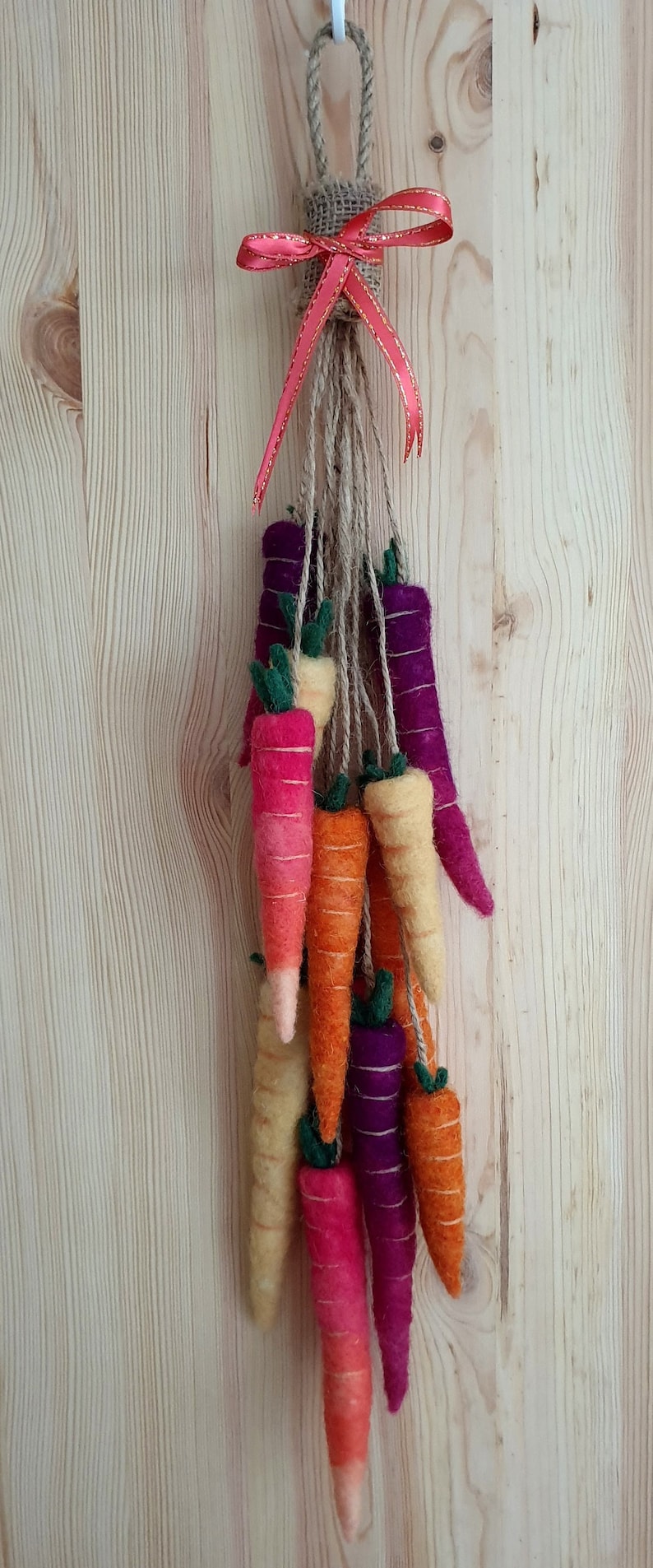 May include: A felt carrot garland with a burlap and red ribbon bow. The garland features a variety of colors, including orange, yellow, pink, and purple.
