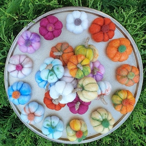 May include: A collection of felt ornaments in various colours and shapes, including flowers, stars, and geometric designs. The ornaments are arranged on a round, wooden surface.