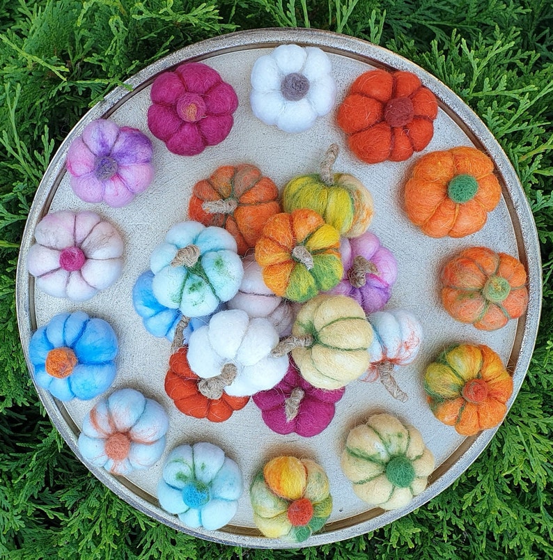 May include: A collection of felt ornaments in various colours and shapes, including flowers, stars, and geometric designs. The ornaments are arranged on a round, wooden surface.