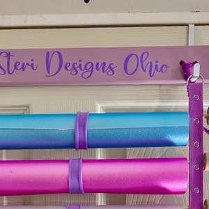 May include: A purple wooden door hanger with the text "Steri Designs Ohio" and two rolls of wrapping paper, one blue and one pink, hanging from it.