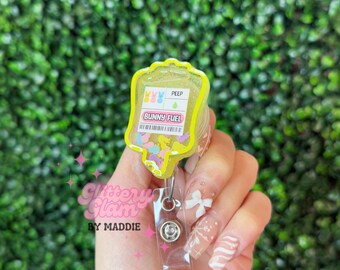 May include: Yellow and clear plastic badge holder shaped like an IV bag with the text "Bunny Fuel" and "Peep" on it. The bag is filled with colorful confetti and glitter.