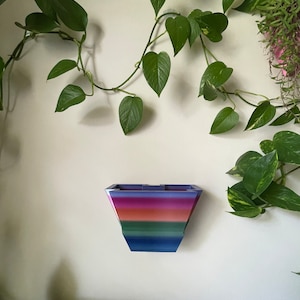 May include: A colourful, geometric wall planter with a rainbow design. The planter is made of plastic and has a modern, minimalist style.