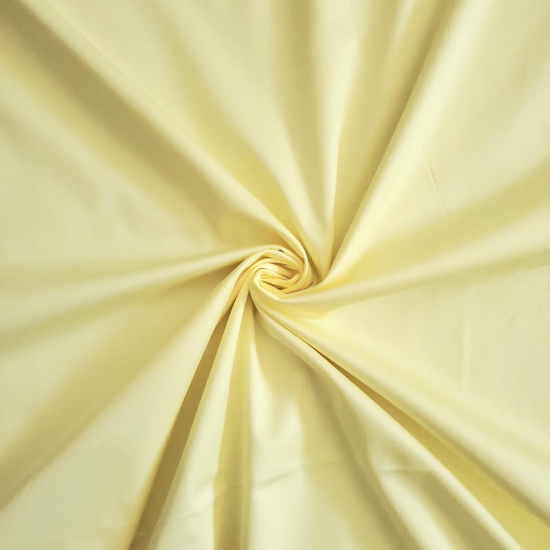 May include: A close-up of a pale yellow fabric with a swirling pattern. The fabric is smooth and appears to be made of a lightweight material. The folds and creases create a dynamic texture, with highlights and shadows adding depth.