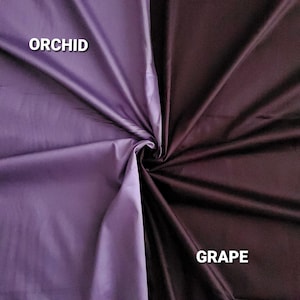 May include: A fabric swatch split into two colours: orchid and grape. Orchid is a light purple, and grape is a deep, dark purple. The fabric is folded in the centre, creating a swirl. The words "ORCHID" and "GRAPE" are printed on the fabric.