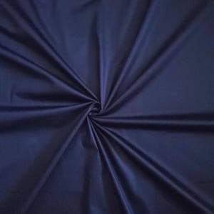 May include: A close-up of navy blue fabric with a glossy finish. The material is gathered in the centre, forming a spiral of folds and shadows. The fabric looks smooth and flowing, ideal for clothing or interior design projects.