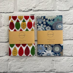 May include: Two cotton handkerchiefs measuring 29cm x 29cm. One features a repeating pattern of red, yellow, and green leaves on a white background. The other displays a floral pattern of blue, grey, and white flowers on a dark blue background.