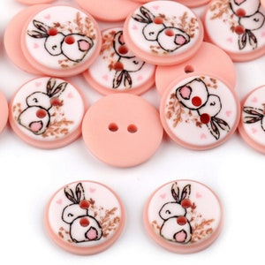 May include: A collection of pink plastic buttons with a white background and a printed design of two bunnies with hearts.