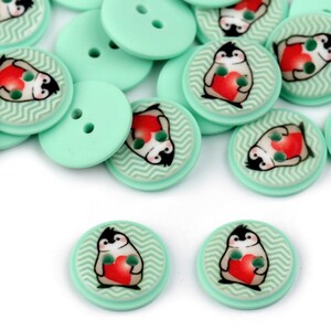 May include: A pile of mint green buttons with a penguin holding a red heart design. The buttons have two holes.