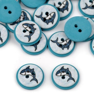 May include: A collection of teal blue wooden buttons with a white background and a cartoon shark design.