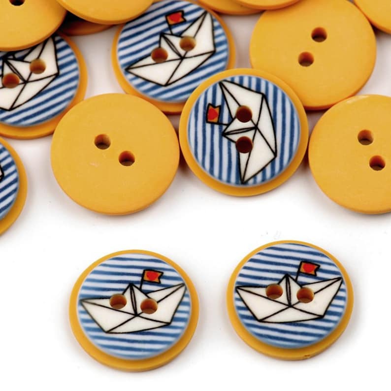 May include: A collection of yellow and blue buttons with a paper boat design. The buttons have two holes and are perfect for sewing projects.