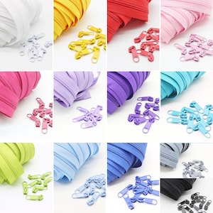 Könnte beinhalten: Sortiment von Reißverschlussbändern in verschiedenen Farben, darunter Weiß, Gelb, Rot, Rosa, Fuchsia, Lila, Hellblau, Dunkelblau, Grün und Grau. Jede Farbe wird mit einem Stapel Metall-Reißverschlussziehern in der gleichen Farbe kombiniert.