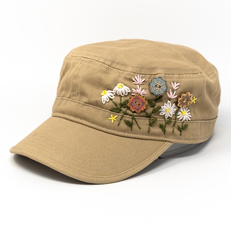 以下が含まれることがあります： 刺繍の花柄が施された、タンカラーのミリタリースタイルのキャップ。 フラットなつばと、しっかりとしたクラウンが特徴です。 花柄の刺繍には、白いデイジー、黄色のアクセント、装飾的なボタンが含まれています。