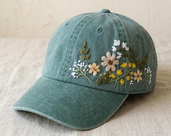 Può includere: Cappellino da baseball turchese con ricamo floreale. Il ricamo presenta fiori bianchi, gialli e beige con foglie verdi. Il cappellino ha una visiera curva e un bottone sulla parte superiore.