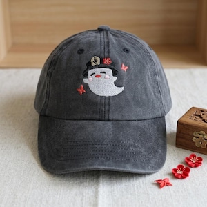Peut inclure: Casquette de baseball gris anthracite avec un motif de fantôme brodé. Le fantôme porte un chapeau noir avec une fleur rouge et est entouré de papillons rouges. La casquette est en tissu doux et a une visière incurvée.