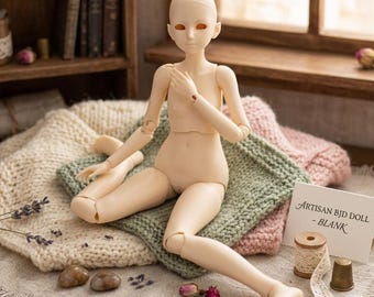 Puede incluir: Una muñeca BJD articulada en blanco, con un tono de piel neutro, sentada sobre una manta de punto verde. La muñeca tiene una cara lisa y sin pintar, rodeada de materiales de artesanía y elementos decorativos. Un letrero dice "Artisan BJD DOLL - BLANK."