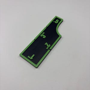 May include: A black and green measuring tool with measurements in inches. The tool has a rectangular shape with a curved edge and green markings indicating 1", 2", 3", and 0.5".