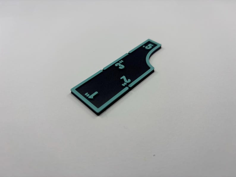 May include: A black and teal-edged ruler with measurements from 1" to 5". The ruler is rectangular with a curved edge on one side. The numbers are teal and are in inches.