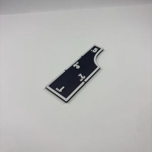 May include: A black and white measuring tool with inch markings from 1" to 5". The tool has a white border and is shaped with a curved edge. The numbers are in white.