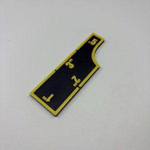 May include: A black and yellow measuring tool with inch markings from 1" to 5". The tool has a unique shape with a curved edge. The numbers and border are yellow, contrasting against the black background.