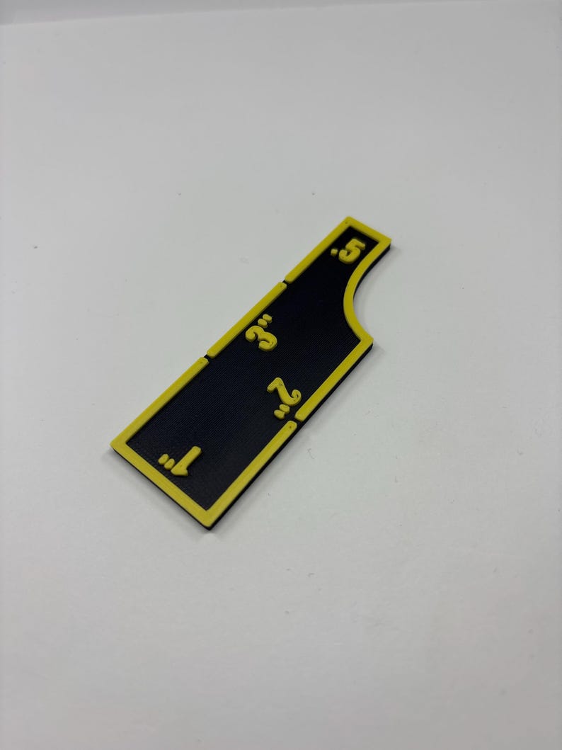 May include: A black and yellow measuring tool with inch markings from 1" to 5". The tool has a unique shape with a curved edge. The numbers and border are yellow, contrasting against the black background.