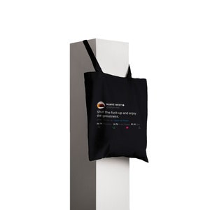 May include: Black tote bag with a white graphic of a tweet from Kanye West that reads "Shut the fuck up and enjoy the greatness."