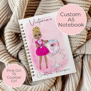 May include: A pink and white A5 notebook with a custom design featuring a cartoon woman in a pink dress holding a pink gin cocktail. The notebook says "Victoria's Cocktail Recipes" and has a pink glitter background.