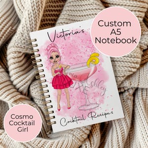 May include: A pink and white A5 notebook with a custom design featuring a cartoon girl holding a pink cocktail with a lemon wedge. The notebook says "Victoria's Cocktail Recipes" on the front.