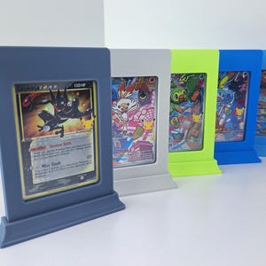 May include: A row of five vertical rectangular plastic display stands in matte blue, gray, lime green, and bright blue, each holding a collectible trading card. The front card features a black Greninja character with the text Greninja 130 HP.
