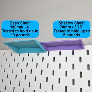 Puede incluir: Un tablero perforado blanco con dos estantes adjuntos. El estante profundo azul mide 100 mm / 4 pulgadas y soporta hasta 10 libras. El estante poco profundo morado mide 70 mm / 2.75 pulgadas y soporta hasta 5 libras, seg&uacute;n las etiquetas de texto.
