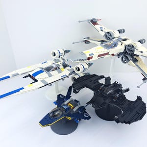 May include: A collection of Star Wars-themed model aircraft, including an X-wing fighter, a Y-wing fighter, a black ship, and a blue and yellow ship. The models are made of plastic and are displayed on white stands.