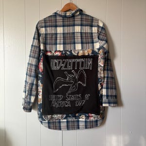 Könnte beinhalten: Ein kariertes Hemd mit einem schwarzen Aufnäher mit dem Led Zeppelin-Logo und einer geflügelten Figur. Das Hemd hat einen floralen Musterakzent und den Text "UNITED STATES OF AMERICA 1977". Das Hemd ist eine Mischung aus Blau, Weiß und Grau.