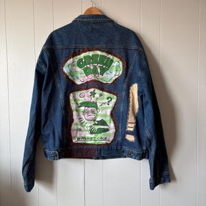 Op de afbeelding: Een witte keramische mok met een zwarte handgreep en de tekst "But First, Coffee" in een vetgedrukte, zwarte letter. De mok staat tegen een wazige achtergrond, wat een gezellige setting suggereert.