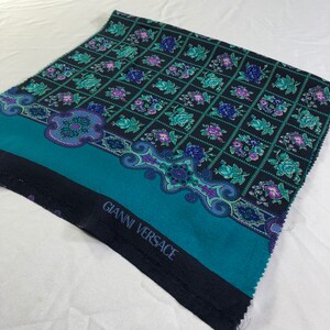 May include: A teal and black fabric with a floral pattern and a border with a paisley design. The fabric has the text "Gianni Versace" printed on it.