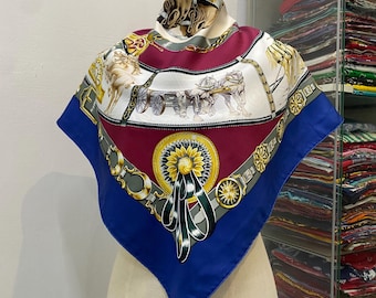 May include: A square silk scarf featuring a central maroon panel with a yellow sunflower and black ribbon motif, surrounded by white sections depicting horse-drawn carriages, and finished with a wide royal blue border and gold chain accents.