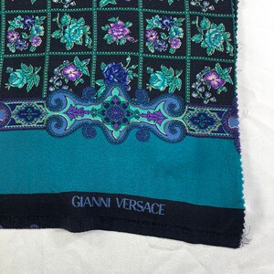May include: Black fabric with a teal blue border and a paisley design. The fabric has a repeating floral pattern in shades of purple, green, and white. The fabric is labelled "Gianni Versace".