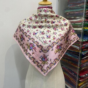 Puede incluir: Un pañuelo de seda con estampado floral rosa y blanco con el texto "Antique Harmonic" en el centro.
