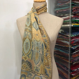 May include: A yellow, blue and brown patterned silk scarf with a paisley design. The scarf is draped around a mannequin's neck.