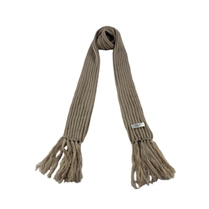 May include: A beige knitted scarf with fringe tassels. The scarf has a small white label with the text "Sakkas" on it.