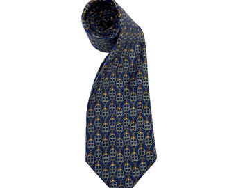 May include: A rolled-up blue tie with a repeating pattern of gold and white interlocking shapes. The tie is made of a shiny fabric and is displayed against a white background. The tie is a classic accessory.