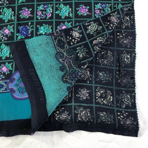 May include: A black and teal fabric with a repeating pattern of floral designs. The fabric has a grid pattern with a floral design in each square. The fabric is folded in half and the text "MADE IN FRANCE" is visible.