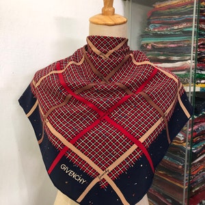 Puede incluir: Un pañuelo de seda azul marino con un patrón geométrico rojo, marrón y blanco. El pañuelo tiene la palabra "Givenchy" impresa.