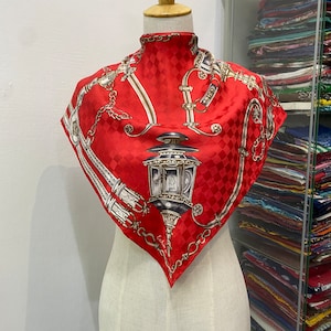 Peut inclure: Un foulard en soie rouge à motif à carreaux et chaîne dorée avec une lanterne. Le foulard porte l'inscription "Echo" dans le coin inférieur droit.