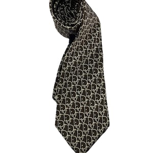 May include: A rolled brown tie with a repeating white pattern. The tie is made of a smooth fabric and is displayed against a white background. The pattern consists of the letters "D" and "R" intertwined.