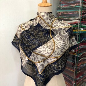 May include: A silk scarf with a navy blue, gold, and white leopard print design. The scarf features a rope pattern and a floral design.