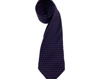 May include: A navy blue tie with a repeating red circular pattern. The tie is rolled at the top and hangs down, showcasing the intricate design. The tie is made of a smooth fabric.