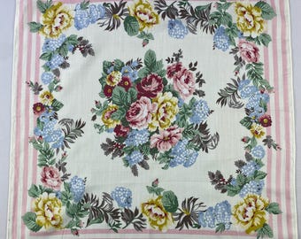 May include: Square white handkerchief with a floral pattern. The handkerchief features a pink striped border and a central bouquet of roses, hydrangeas, and other flowers in shades of pink, yellow, and blue. A small logo is visible in the corner.
