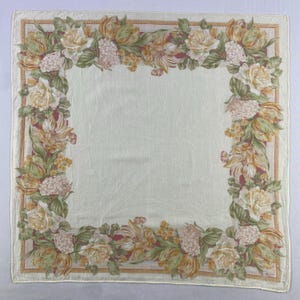 May include: A white silk scarf with a floral border. The border features yellow, orange, and pink flowers with green leaves. The scarf is trimmed with a gold border and has the word "Liberty" printed in the bottom right corner.