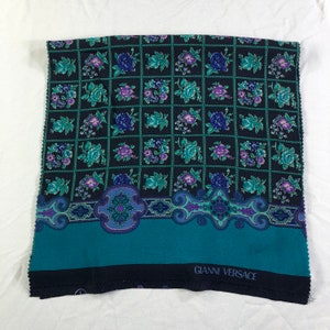 May include: A teal and black fabric with a floral pattern and a border. The fabric has the text "GIANNI VERSACE" printed on the bottom.
