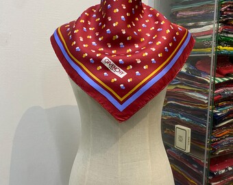 Könnte beinhalten: Ein roter Seidenschal mit blauem und gelbem Rand und einem weißen und roten Tupfenmuster. Der Schal trägt den Aufdruck "Givenchy Paris" in der Mitte.